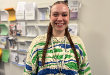 megan wagenblast is wearing a white, blue and green sweater and has her hair in two long pony tails. She is pictured in the AWHS counseling office